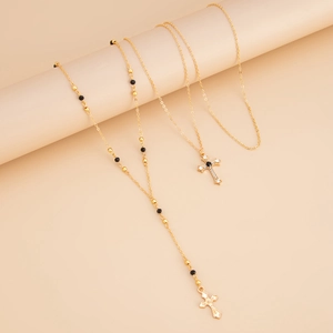 Détail de parure de colliers dorés avec pendentifs croix en cristal et chaînes à billes