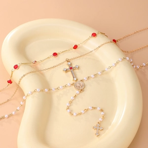 Détail du collier doré multicouche avec pierres rouges, perles et pendentifs de croix