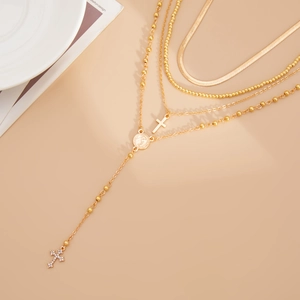 Détail de colliers dorés superposés avec pendentifs croix et pièce sur fond chaud