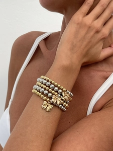 Detail of layered gold and silver bead bracelets with delicate bow charms on wrist