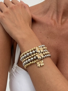 Detailed view of layered gold and silver bead bracelets with bow-knot charms on wrist