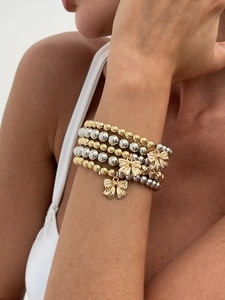 Detail of layered gold and silver bead bracelets with bow pendants on a model's wrist