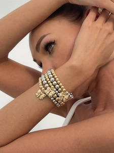 Detail of layered gold and silver beaded bracelets with a delicate bow charm on wrist