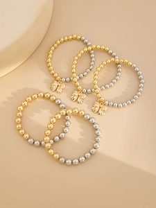 Detail of 5-piece beaded bracelet set with gold bow charms on minimalist stands