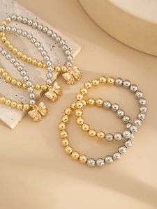 Detail view of stacked gold and silver beaded bracelets with metallic bow pendants on stones