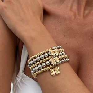 Chic layered beaded bracelet set with gold and silver balls and bow charms on wrist