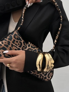 Close-up of chunky gold bangle set and ring paired with a leopard print saddle handbag