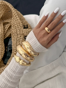 Detailed view of layered gold chunky bracelets and minimalist domed ring on a model