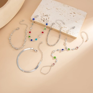 Detail von silberner Schlangenkette und buntem Edelstein-Armband-Set auf Steinfläche
