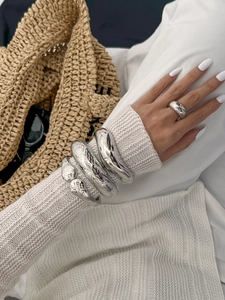 Close-up of minimalist silver irregular metal bangles and ring on a model in white outfit