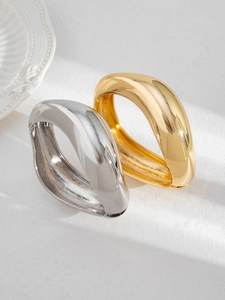 Macro view of wide irregular polished gold and silver metal bangles with mirror finish