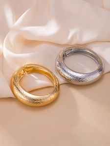 Detailed close-up of gold and silver metallic bracelets with wheat ear textured engraving
