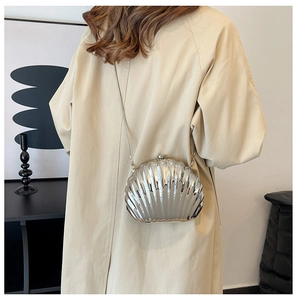 Silver shell-shaped metallic clutch bag with chain strap shown on a woman in a coat