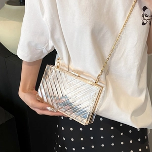 Minimalist transparent acrylic box bag with gold chain strap shown on model in home setting