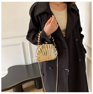 Detailed view of a gold shell-shaped clutch with bead handle and chain strap