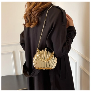 Golden shell-shaped evening bag shown on a model, featuring a beaded handle and metal chain