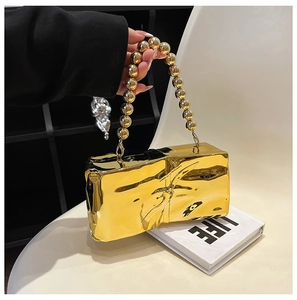 Detail of gold wrinkled clutch bag with large metallic bead handle held by hand