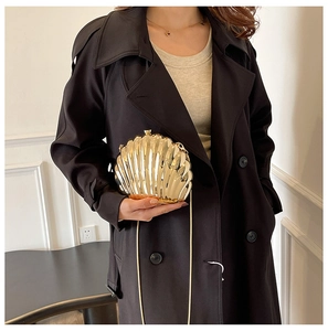 Elegant gold shell evening clutch bag with chain strap shown on black coat outfit