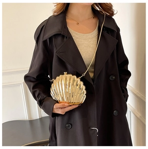 Golden shell-shaped evening bag with metallic finish and chain strap on a model