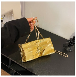 Detail of gold metallic clutch bag with large bow and elegant bead chain strap