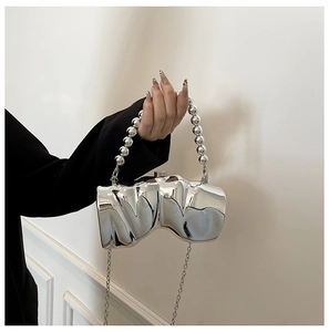 Detail der silbernen metallischen Clutch in unregelmäßiger Form mit Perlengriff und Kette