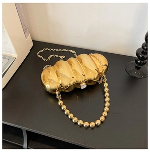 Detail of gold wavy acrylic clutch bag with metallic mirror finish and beaded handle