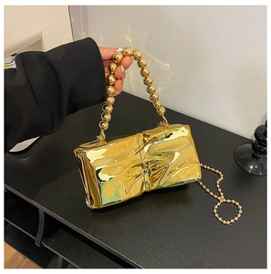 Detail of gold mirror finish handbag with twisted pleats and beaded handle texture