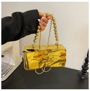 Detail of elegant gold quilted mini bag with glossy metallic finish and beaded handle