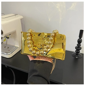 Detailed view of gold metallic clutch bag with wrinkled texture and bead handle