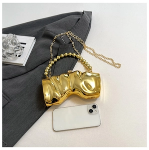 Detail der goldenen Metall-Clutch mit Perlengriff und Kettenriemen sowie Handy als Maßstab