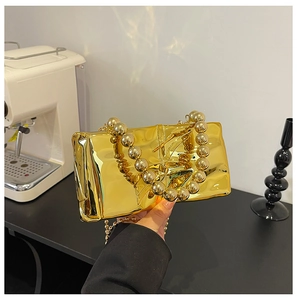 Detail of a gold mirror-finish clutch bag with a unique large round bead handle strap