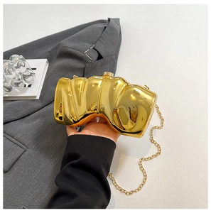 Makroaufnahme einer goldfarbenen Abendtasche mit Wellenstruktur und langer Metallkette