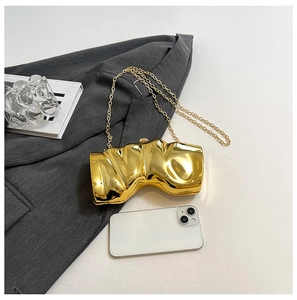 Detailansicht der unregelmäßigen goldenen Clutch mit Metallkette auf grauem Blazer