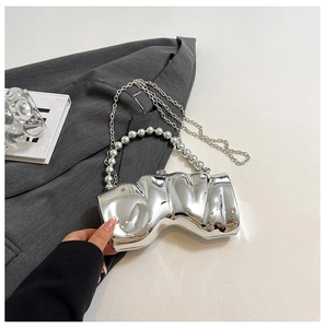 Detail einer silbernen Abendtasche in Wellenform mit Perlenhaube und Metallkette