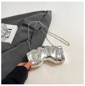 Detail der silbernen Metallic-Clutch in Muschelform mit gewellter Textur und Kette