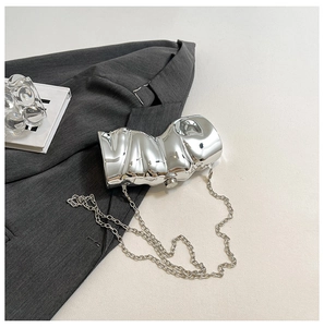 Detail der silbernen, unregelmäßigen Spiegel-Clutch auf einem grauen Blazer für den Abend