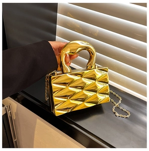 Close-up of golden box clutch bag with quilted texture and chunky metal handle