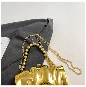 Detailaufnahme der goldenen Abendtasche mit Wellenstruktur und Perlenhandgriff