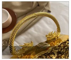 Detail of golden acrylic clutch bag with ornate dragon handles and rippled texture