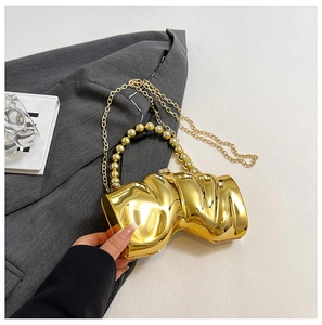 Nahaufnahme der goldenen Shell-Clutch mit Perlengriff auf einem grauen Sakko