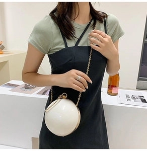 Detail view of a white spherical clutch bag with golden metal ring handle and chain strap
