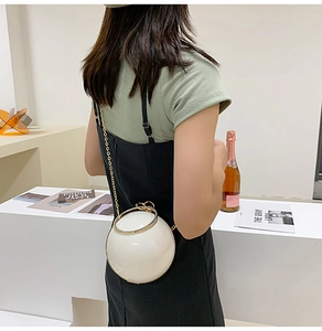 Close-up of a white spherical evening bag with golden ring handle and chain strap