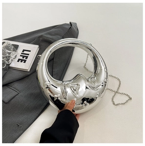 Detail of silver crescent moon clutch bag with liquid metal texture on a grey blazer