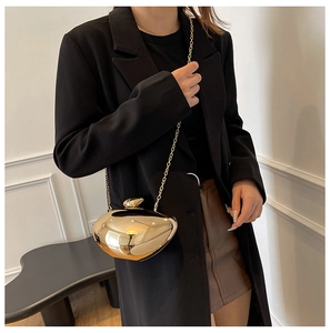 Model wearing a gold heart-shaped metal clutch bag with a sleek acrylic chain strap