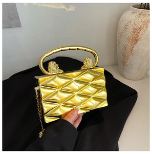 Detail of golden quilted hard-shell clutch bag featuring a lion head carving and thin chain
