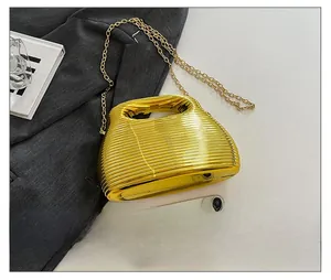 Close-up of golden metallic chain bag with ribbed texture shown next to a smartphone