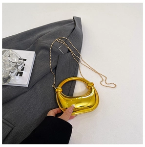 Detail der goldenen Metallic-Halbmond-Abendtasche mit Rundgriff auf grauem Blazer