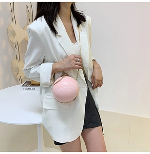 Detail of pink spherical bag with pearl luster and golden chain worn with a white blazer