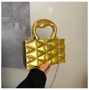 Detail of a gold metallic box bag featuring a 3D quilted texture and rounded handle