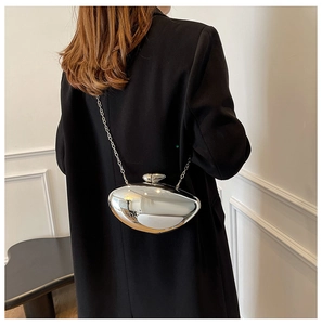 Polished silver metal oval clutch bag with thin chain strap worn on black blazer